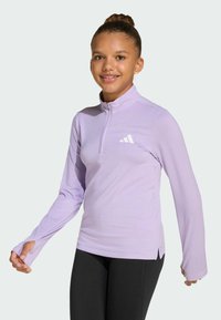 Light purple long-sleeve pullover with a half-zip collar, soft fabric, and a white logo detail on the left chest. Black leggings are worn.