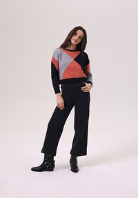 Pull coloré à motifs géométriques avec des sections rouges, grises, noires et blanches. Associé à un pantalon noir taille haute et des bottines noires.