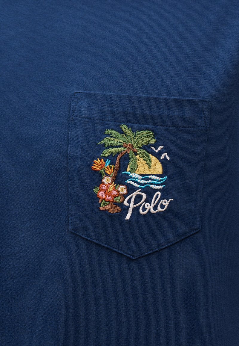 Zak van een marineblauw overhemd met borduursel van een palmboom, bloemen, oceaangolven, vogels en het woord "Polo" in sierletters.