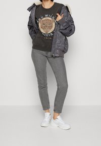 Šedá bomber bunda s fleece podšívkou, grafická černá mikina s potiskem lva, šedé skinny džíny a bílé tenisky.