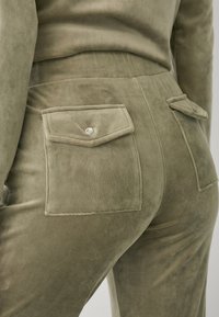 Olijf groene suède broek met een gladde textuur, voorzien van twee achterzakken met puntige kleppen en zilveren drukknoopsluitingen.