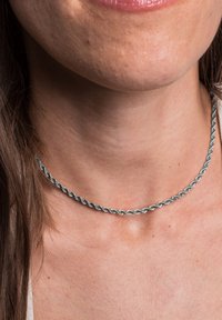 Hõbedane keerdnekaelakee, millel on sile metalline tekstuur, tihedalt kaela külge sobiv, omades lihtsat ja elegantset disaini.