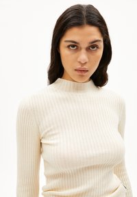 Lys beige ribbet langærmet top med en høj hals, lavet af et struktureret strikstof med subtile lodrette linjer.