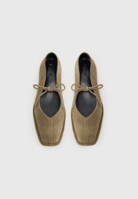 Ballerines en suede vert olive avec un bout carré, des découpes sur les côtés et un nœud à l'avant. Doublure et couture noires visibles.