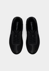 Baskets noires Calvin Klein avec lacets, accents en cuir et semelle intérieure marquée, vues de dessus sur un fond blanc.