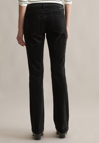 Zwarte fluweelachtige corduroy broek met een rechte pasvorm, voorzien van achterzakken en een gestructureerde stof. De tailleband is iets verhoogd.