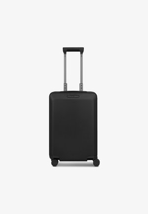 Valise rigide noire avec poignée télescopique déployée et quatre roues pivotantes, face avant avec plaque logo Porsche Design.