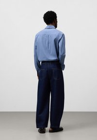 Ljusblå långärmad skjorta med ett bakstycke, i kombination med mörkblå vida jeans. Svarta skor fulländar outfiten.