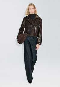 Braune Lederjacke in Kurzform mit Reverskragen, Reißverschluss und Fronttaschen, kombiniert mit weitem, dunkelblauem Jeanshose.