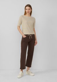 Pasiasty beżowo-biały top z krótkim rękawem w połączeniu z brązowymi spodniami prostymi. Kremowe trampki uzupełniają całość. Prosty design, casualowy wygląd.