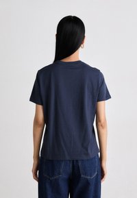 Navy blue cotton t-shirt with a relaxed fit, short sleeves, and a crew neckline, paired with high-waisted denim pants. Simple design.