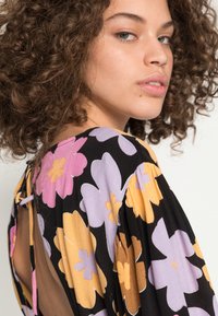 Vestido floral preto com grandes flores rosas, roxas e laranja. Tecido suave com uma abertura nas costas em forma de lágrima e detalhe de laço na gola.