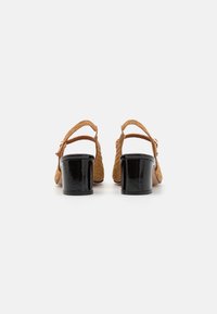 Brown woven sandals with a back strap and a shiny black block heel, featuring textured material and adjustable buckle closure.