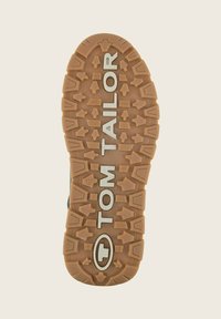 Suela de zapato de goma en tono marrón con un patrón de relieve texturizado y multidireccional. Presenta "TOM TAILOR" impreso en plata a lo largo del centro.