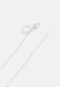 Silver chain necklace with a textured round clasp. Features links of varying shapes and a prominent decorative ring attached to the clasp.
