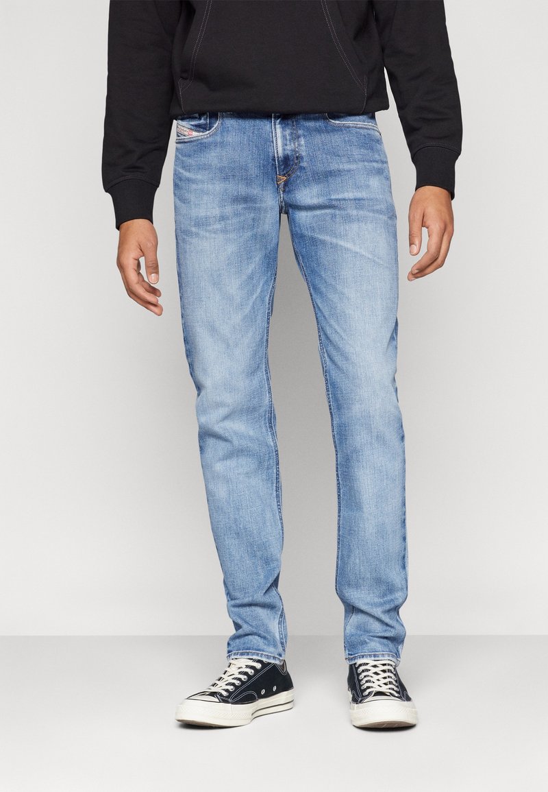 Jeans de mezclilla azul claro con un corte ajustado, diseño de cinco bolsillos, acentos cosidos y cierre de botón. Llevados con zapatillas negras.