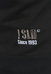 Schwarzer Sweatshirt mit gesticktem Text "!SLD" in Grau und "Since 1993" in Weiß, das eine gerippte Textur aufweist.