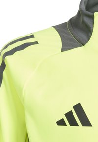 Neongele sportjack met grijze accenten. Kenmerken zijn een hoge kraag, drie zwarte strepen op de schouder en een prominent zwart logo.