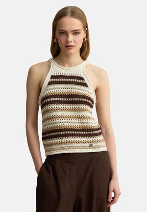 Mujer con top de crochet sin mangas con rayas horizontales marrones, beige y crema y pantalones marrón oscuro sobre fondo blanco.