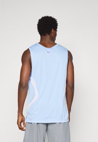 Helles blaues ärmelloses Sporttrikot aus strukturiertem Mesh-Material, mit lila Nike-Logo auf der Rückseite und hellgrauen Akzenten an den Seiten.
