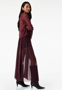 Bordeaux laagjasje met een doorschijnende overlay en een bijpassende lange mouwjasje, gecombineerd met zwarte puntige enkellaarsjes.