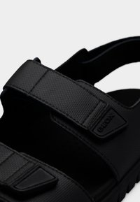 Μαύρο σανδάλι με υφή στο πάνω μέρος, ρυθμιζόμενους ιμάντες και λαστιχένια σόλα. Το λογότυπο της Geox εμφανίζεται στη πλευρά. Σχεδιασμένο για αναπνευσιμότητα και άνεση.