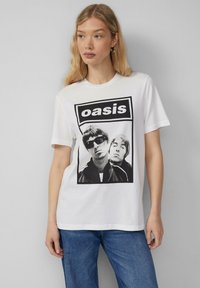 White cotton T-shirt featuring a black and white graphic print of two musicians with the text "oasis" in a bold, rectangular logo.