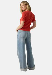 Haut tricoté rouge à manches courtes et à motif texturé, associé à un jean à jambes larges bleu clair avec un ourlet retourné et des poches arrière.
