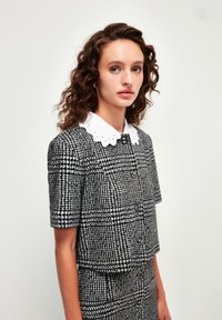 Zwart-wit geblokt tweedelig outfit met korte mouwen en een witte scalloped kraag. Textuurstof met een knoopdetail.