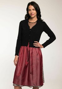 Schwarze Strickjacke mit V-Ausschnitt, ausgestattet mit einem strukturierten Muster und Knöpfen. Kombiniert mit einem glänzenden roten Satinrock, der mit einem gemusterten Saum akzentuiert ist.