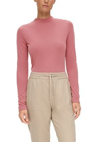 Haut à manches longues en tissu côtelé rose doux, avec un col montant. Associé à un pantalon beige à cordon de serrage en matériau doux.