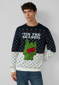 Granatowy sweter z białymi i zielonymi wzorami świątecznymi. Na przodzie zielone pudełko na prezent z napisem „NIE OTWIERAĆ DO ŚWIĄT” na czerwono. Wykonany z mieszanki bawełny.