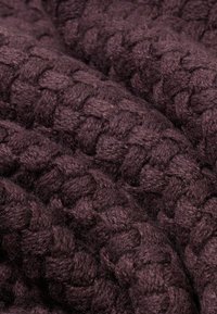 Dunkelvioletter gestrickter Stoff mit einem dicken, strukturierten Muster, das eng gewebte Zöpfe zeigt und ein gemütliches, voluminöses Aussehen erzeugt.