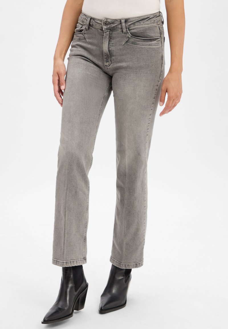 Graue Denim-Jeans mit geradem Schnitt, ausgestattet mit Fronttaschen und einem Knopfverschluss. Getragen mit schwarzen, hohen Ankle Boots.