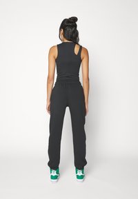 Svart ärmlös topp med cut-out på ryggen, kombinerad med svarta joggers och sneakers med gröna sulor, som visar upp en avslappnad sportig stil.