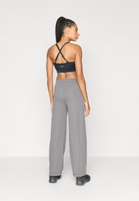 Μαύρο αθλητικό μπουστάκι με λουριά που διασταυρώνονται στην πλάτη και γκρι παντελόνι φόρμας με φαρδιά μπατζάκια. Το μπουστάκι διαθέτει λογότυπο· το παντελόνι έχει ελαστική μέση και λεία υφή.