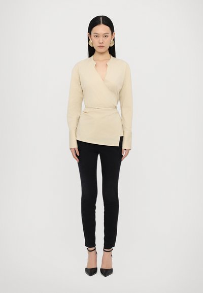 Beige wrap blouse with long sleeves and a deep V-neck, paired with black skinny pants and black pointed-toe heels. Smooth fabric texture.