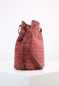 Rød tekstureret stofskuldertaske med brune læderdetaljer, snørelukning og gyldne betræk, der viser et geometrisk mønster.