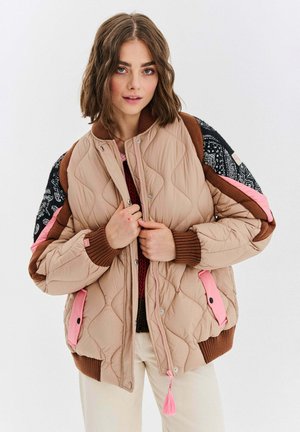 Puchowa bomberka w jasnym beżu z wzorzystymi rękawami, różowymi akcentami i prążkowymi mankietami. Posiada zamek błyskawiczny oraz dekoracyjną frędzel.