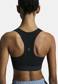 Soutien-gorge de sport noir avec un design dos nageur et un tissu lisse. Présente un petit logo au dos et une silhouette ajustée.