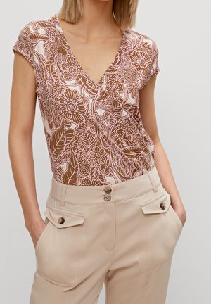Haut marron à motif floral avec un décolleté en V et des manches courtes, assorti à un pantalon beige taille haute avec des poches décoratives et des boutons.