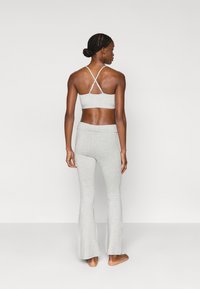 Γκρι bralette με λεπτές τιράντες διαθέτει σχεδιασμό με διασταυρούμενη πλάτη, συνδυασμένο με γκρι κολάν με φαρδύ τελείωμα, και τα δύο από απαλό, λείο ύφασμα.