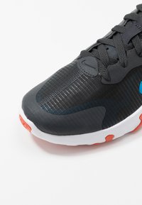 Baskets noires avec une tige en mesh texturé, un col rembourré et des accents gris. Semelle blanche avec des inserts orange et un détail logo distinctif.