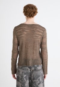 Langærmet, let sweater i en dæmpet brun nuance med et tekstureret, stribet mønster. Kombinationen er med grå, mønstrede bukser med vidde.