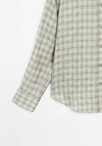 Lichtgroene geruite blouse van soepel materiaal, met lange mouwen, knoopsluiting aan de voorkant en een gebogen zoom. Kleine witte en donkerdere groene vierkantjes.