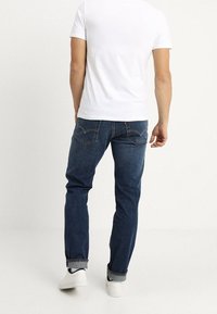 Granatowe dżinsy z prostymi nogawkami, z tylnymi kieszeniami i podwiniętymi mankietami, w zestawieniu z gładką białą koszulką i białymi trampkami.