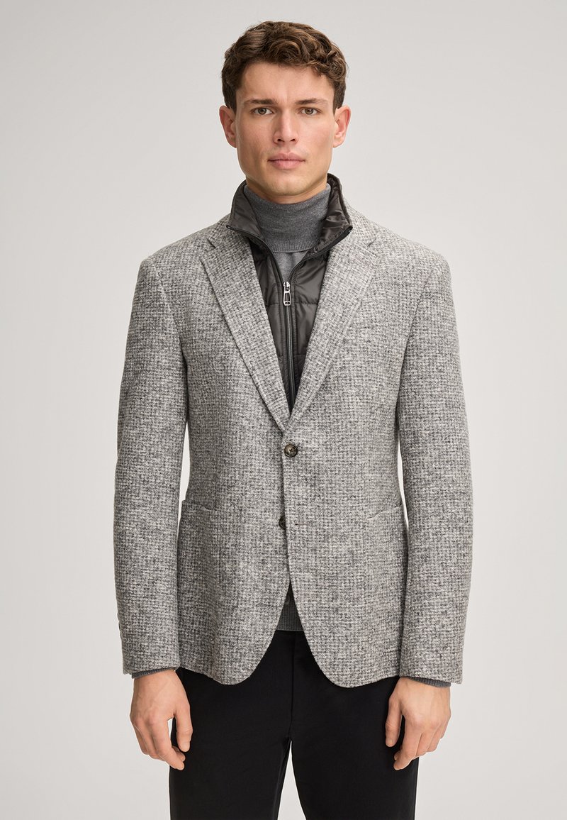 Grauer gewebter Blazer mit strukturiertem Muster, ausgestattet mit zwei Fronttaschen und einem Ein-Knopf-Verschluss, übereinander getragen mit einer schwarzen Jacke mit Reißverschluss.