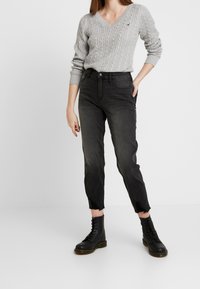 Gray cable-knit sweater with a V-neck, paired with black high-waisted jeans featuring frayed hems and black lace-up boots.