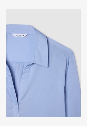 Blusa azzurro chiaro con colletto, chiusura con bottoni e un tessuto morbido e strutturato. Presenta delle pieghe sul davanti per una vestibilità comoda.