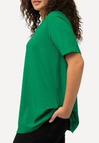Zielona koszulka z krótkim rękawem, wykonana z miękkiego materiału, o luźnym kroju i okrągłym dekolcie. Połączona z czarnymi spodniami.